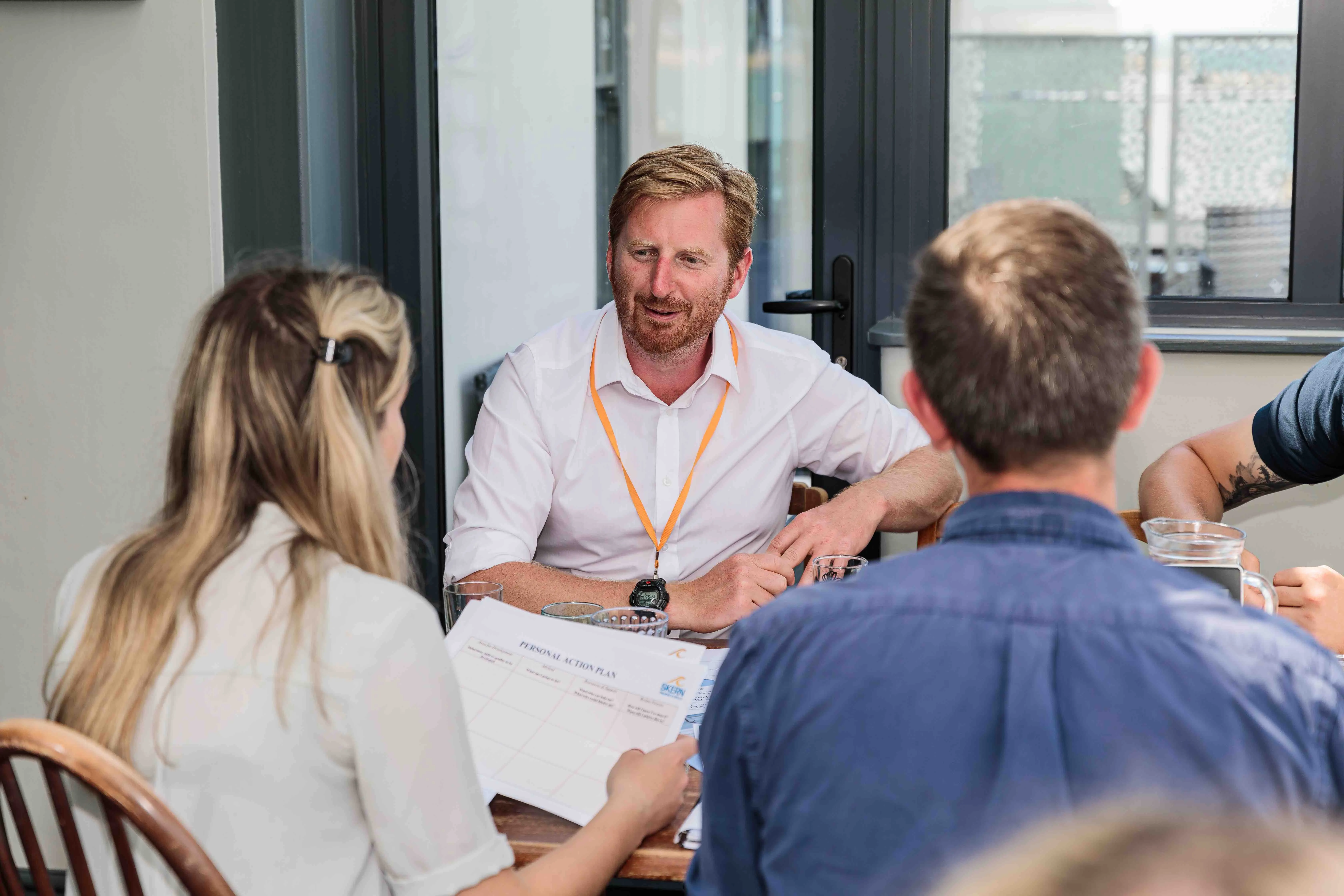 Three people having a discussion around a table, one holding a document titled Personal Action Plan.