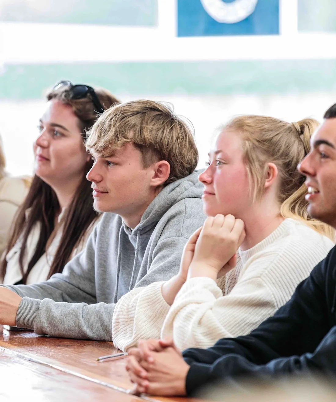 Four young adults sitting side by side at a table, attentively looking forward.