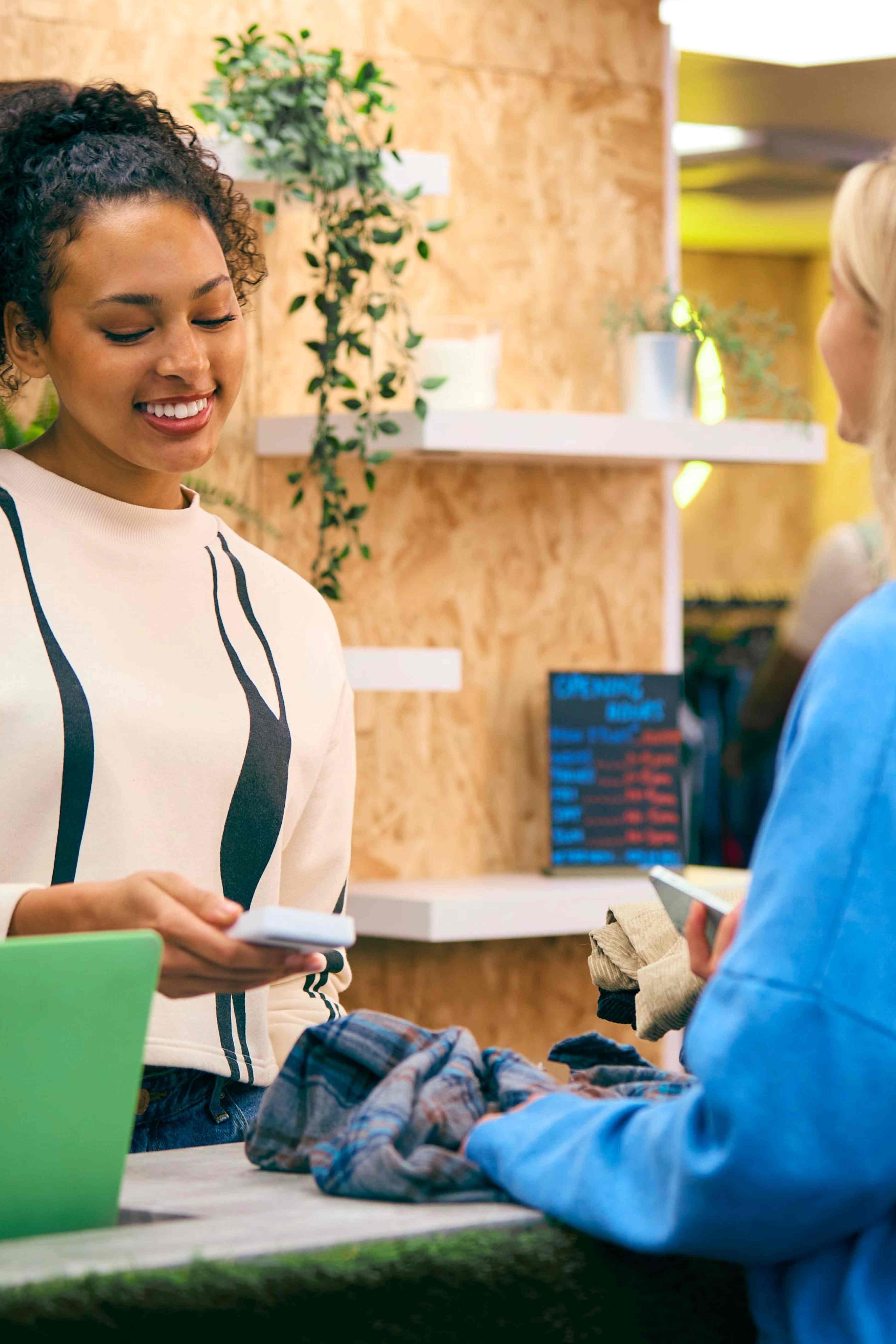 Smiling cashier scanning clothes for a customer at a store counter.