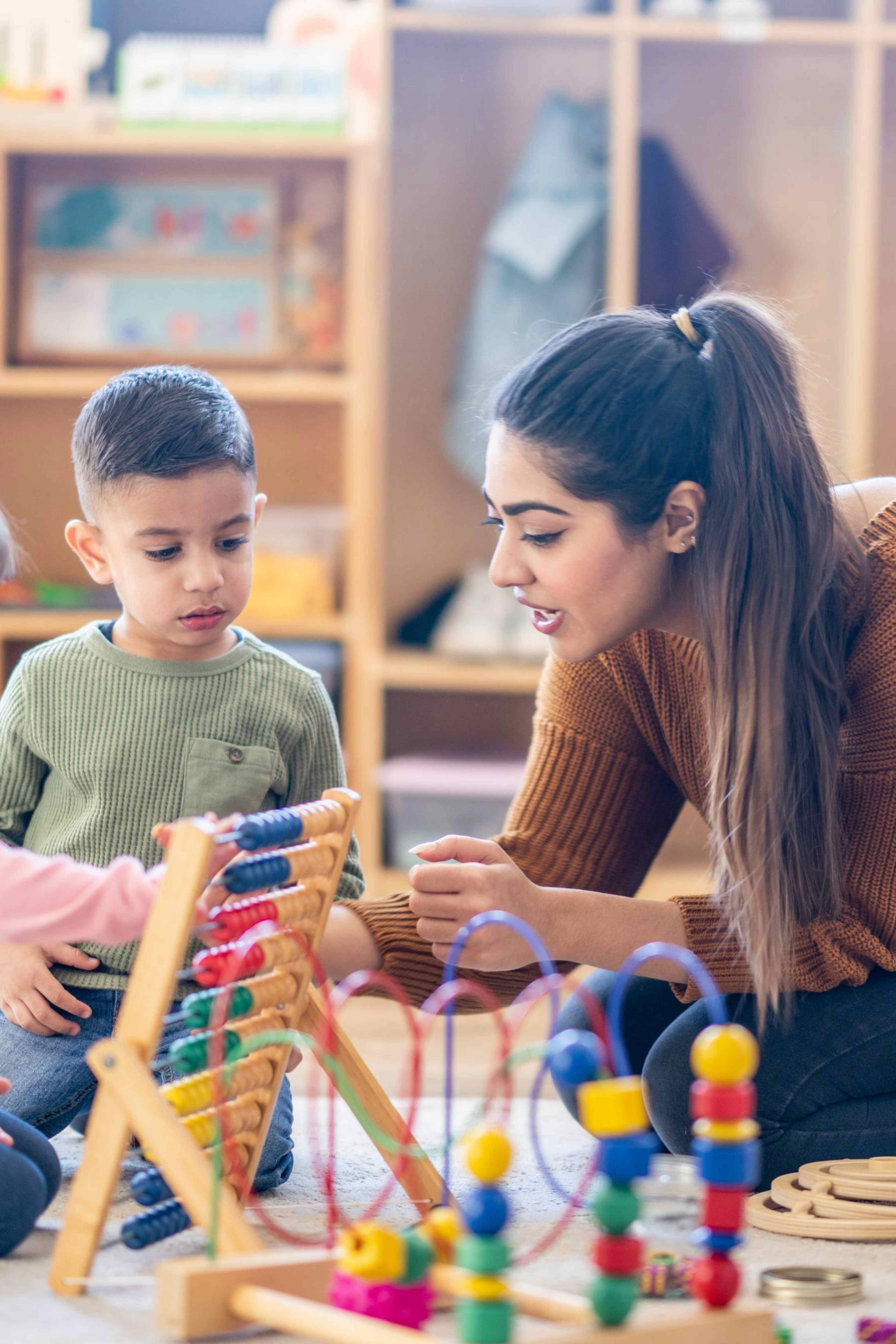 Young boy and woman playing with colorful educational toys in a classroom setting.