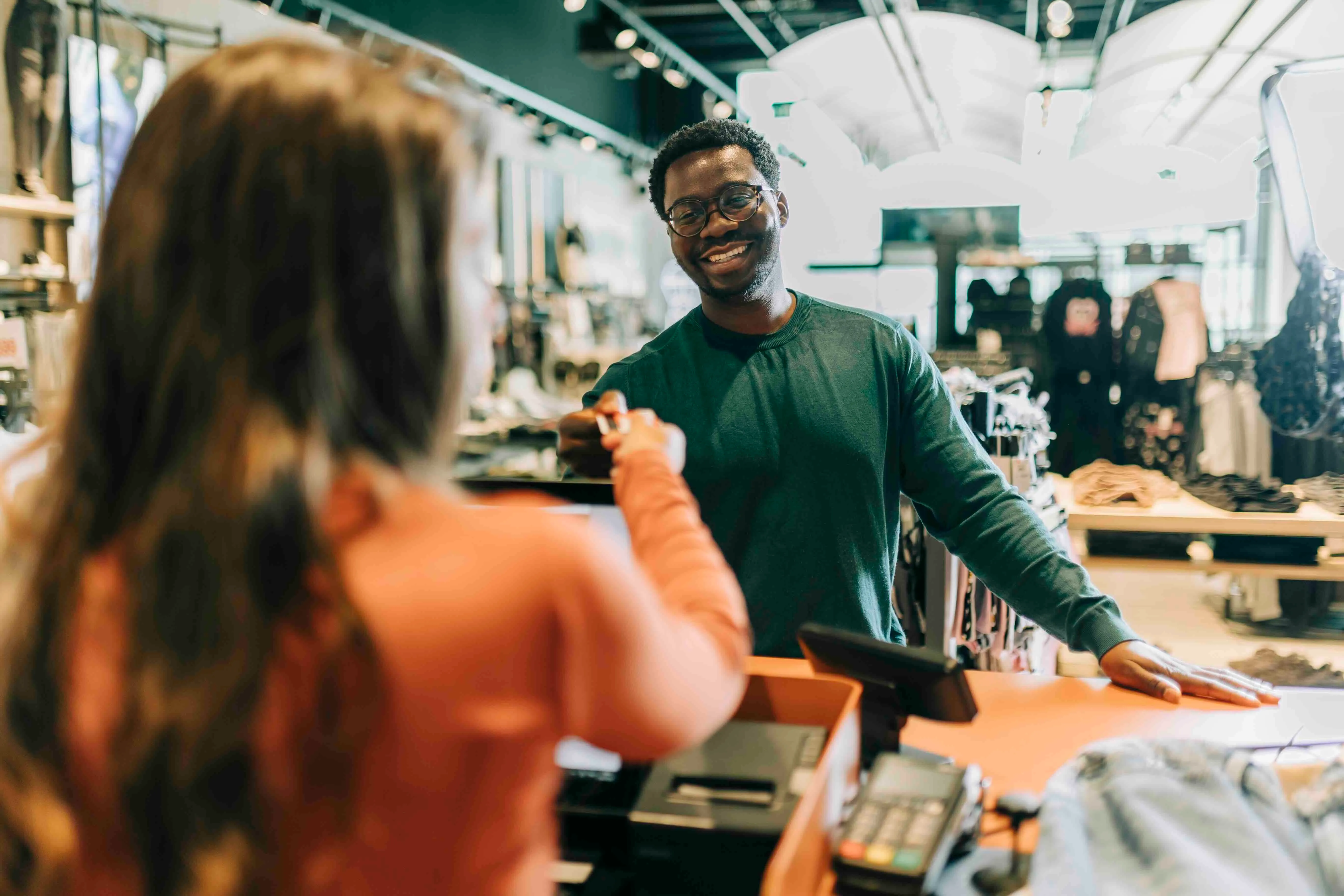 Smiling male cashier handing a customer a credit card in a clothing store.