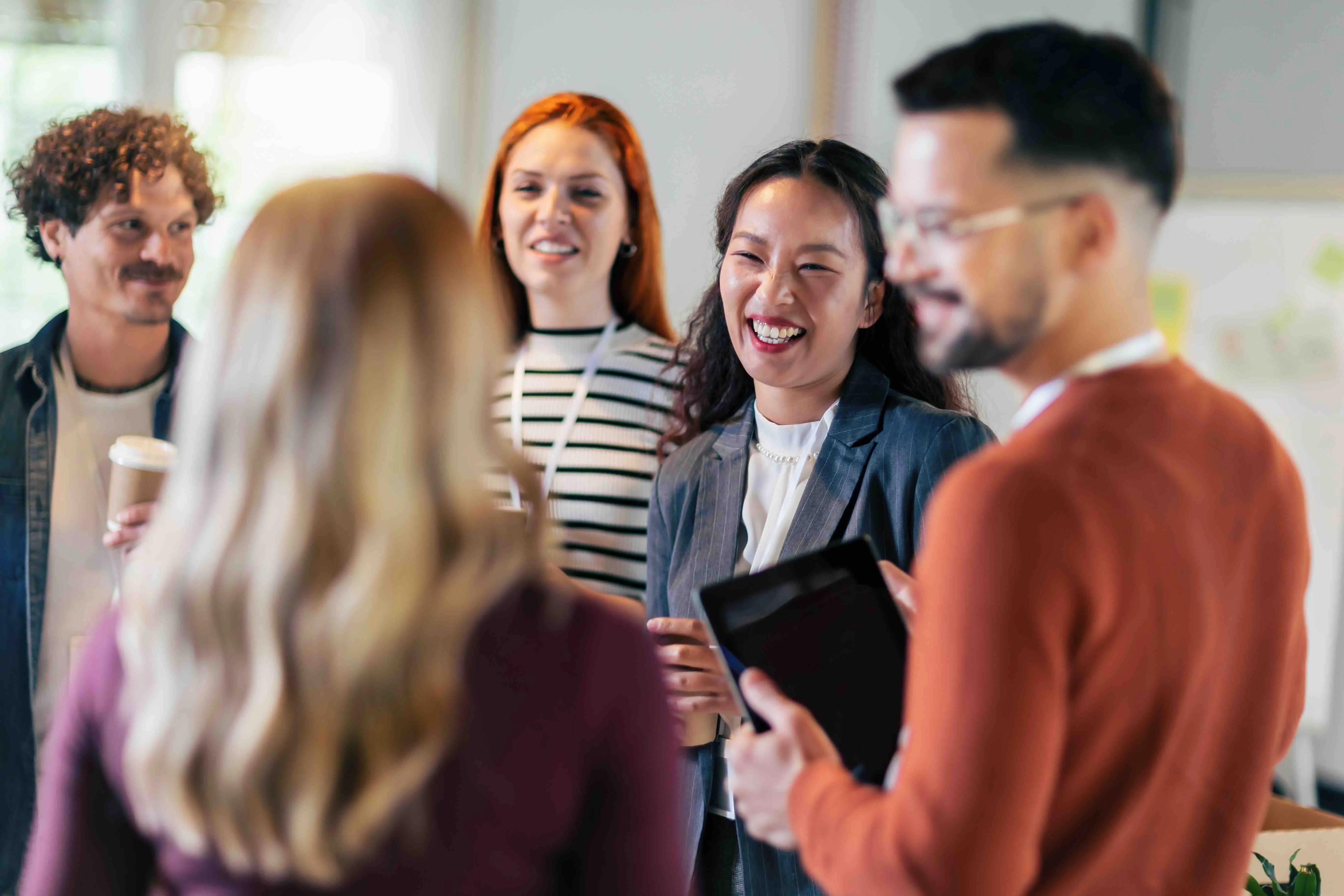 A group of five diverse colleagues smiling and chatting in an office setting.