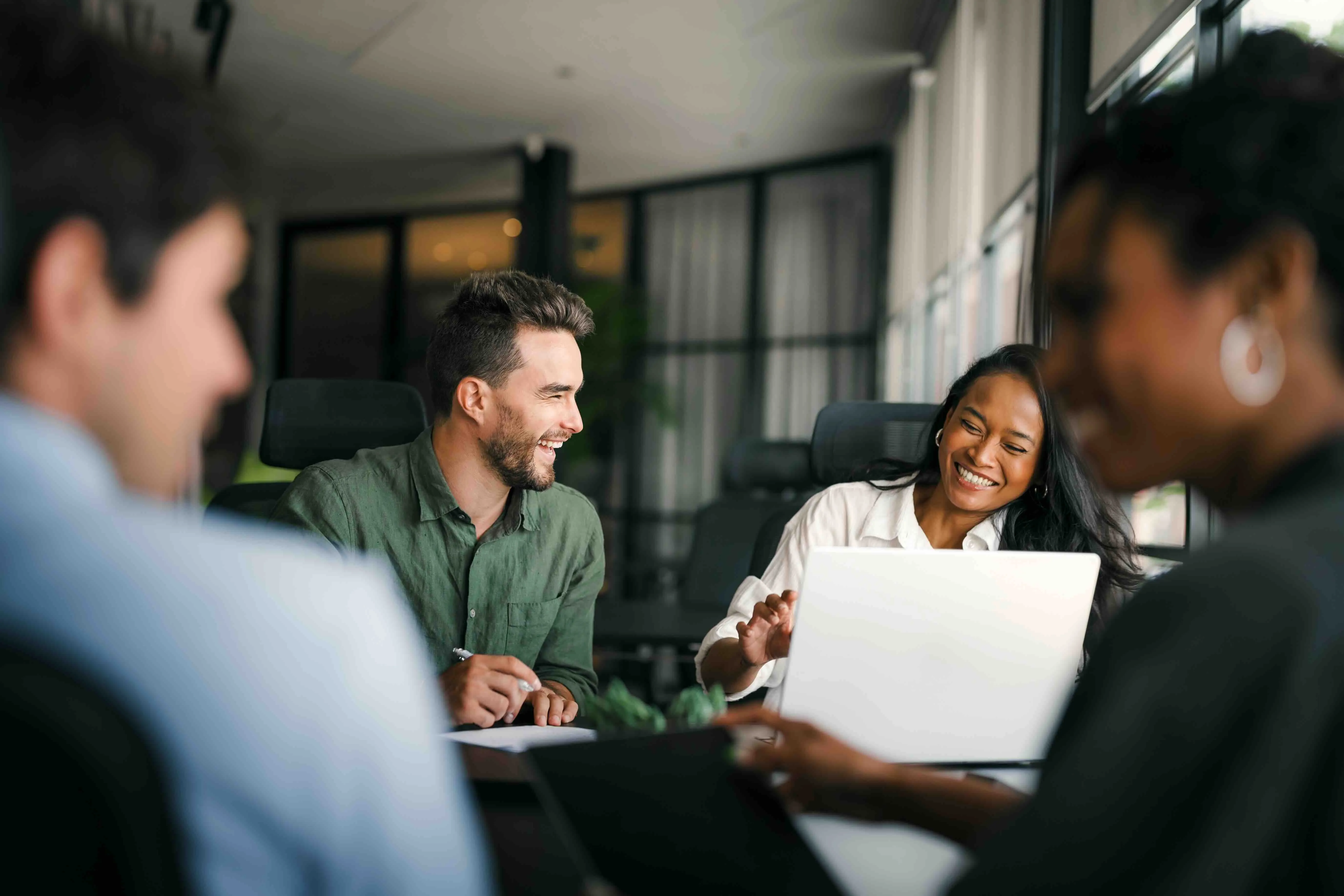 Group of four diverse professionals smiling and collaborating around a table with laptops in a modern office.