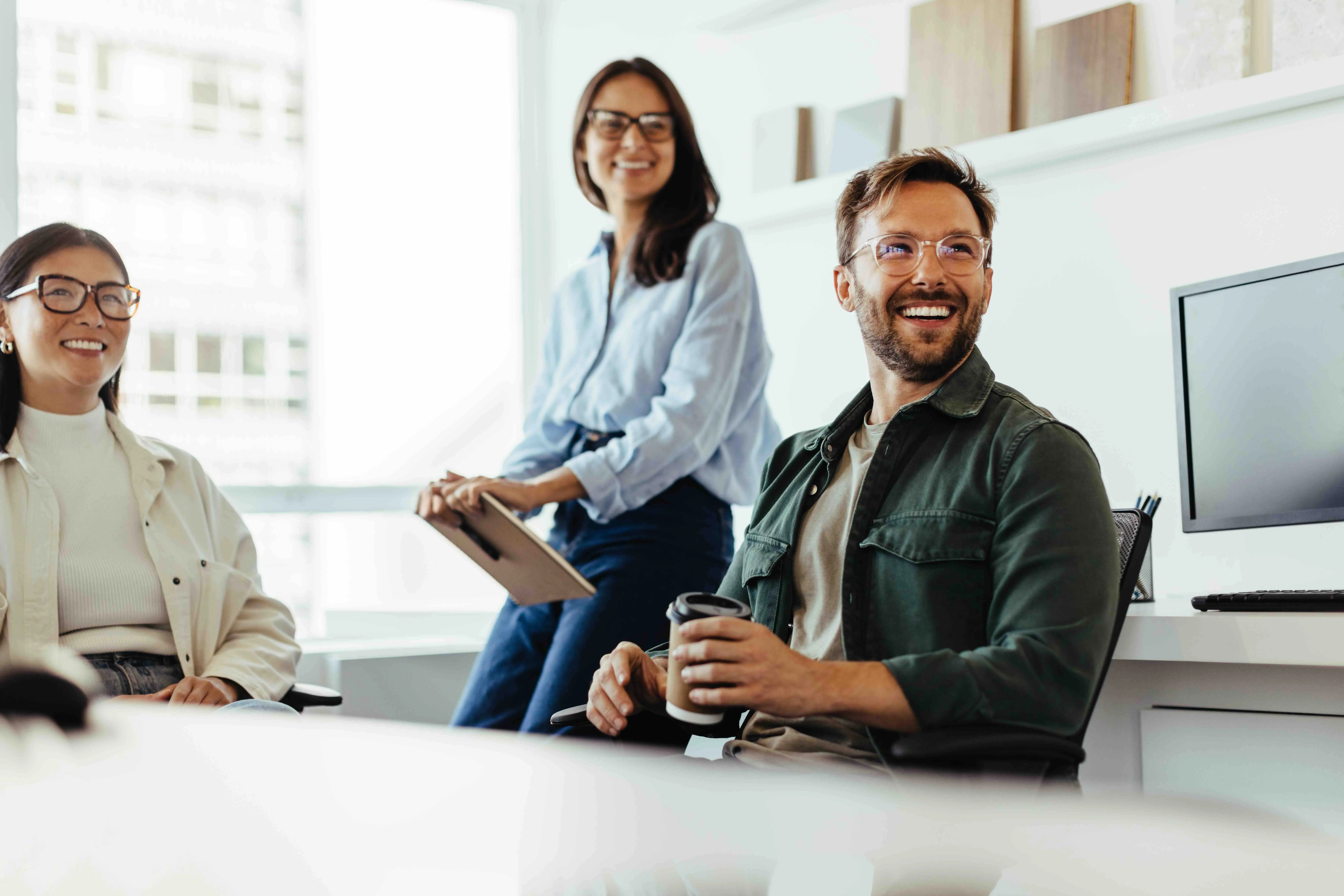 Three young professionals with glasses smiling and interacting in a bright modern office.