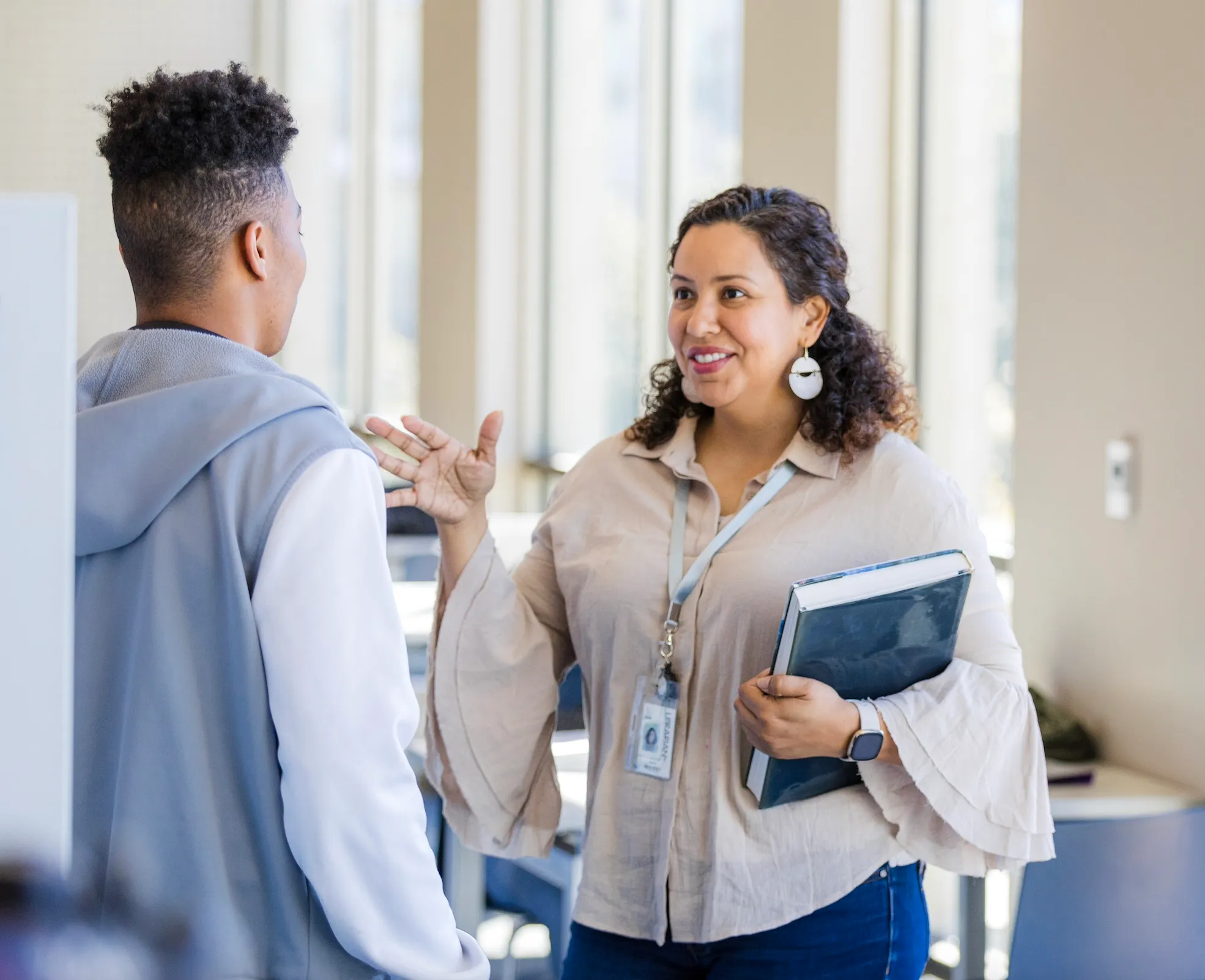 Woman holding a book and talking to a young man in a bright office setting.