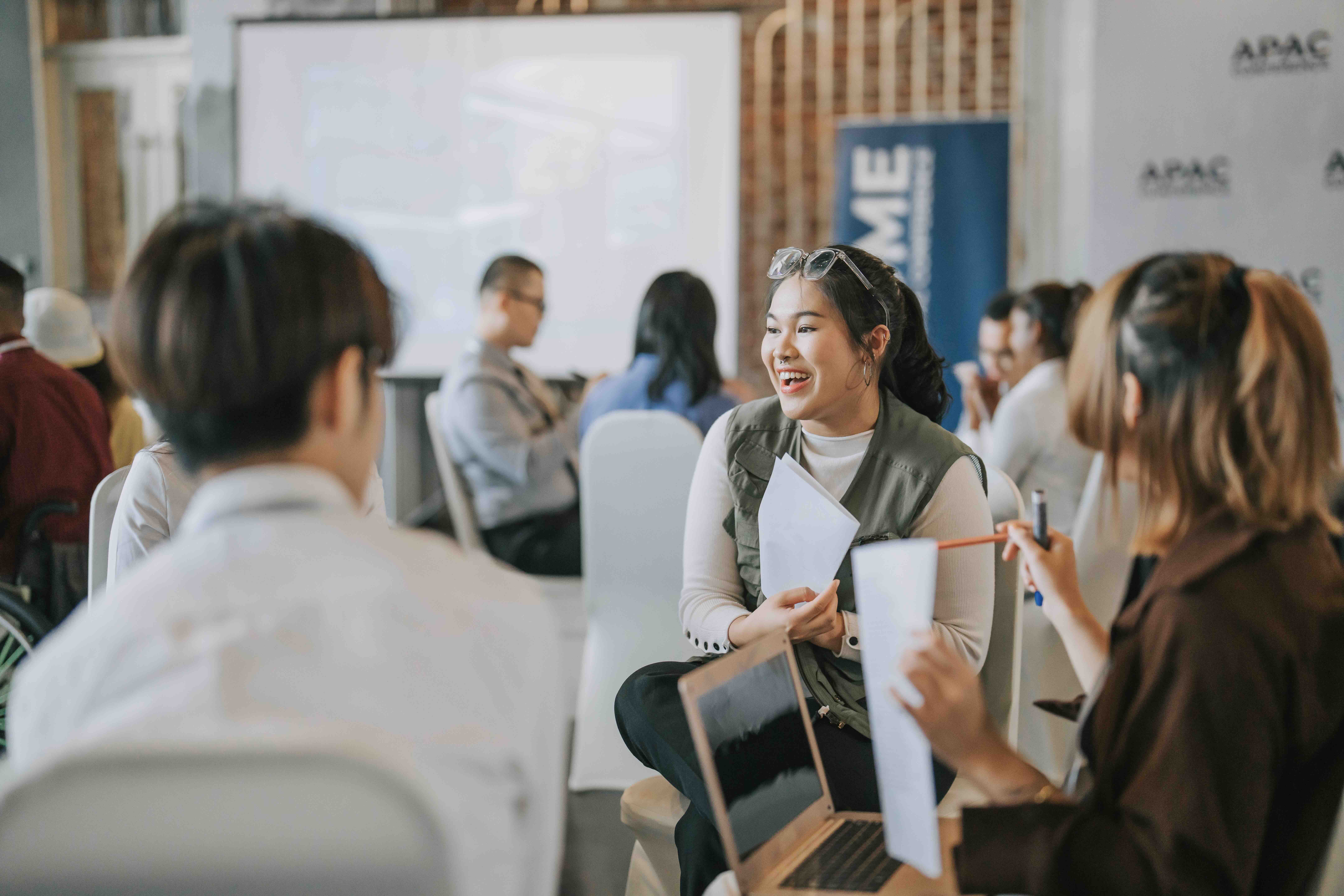 Group of diverse young adults having a discussion in a casual meeting setting with laptops and papers.