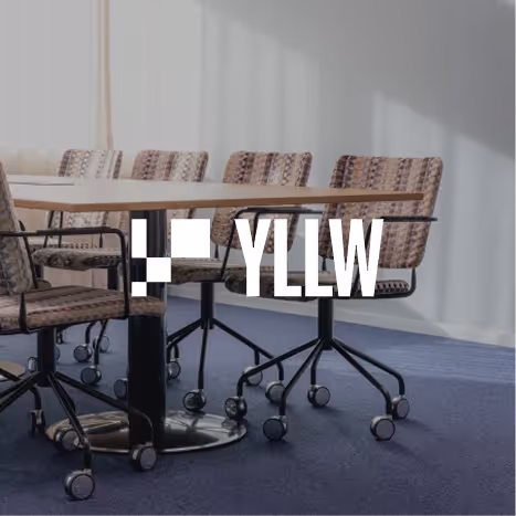 Modern office conference table surrounded by rolling chairs on a blue carpet with sunlight casting shadows on a gray wall.