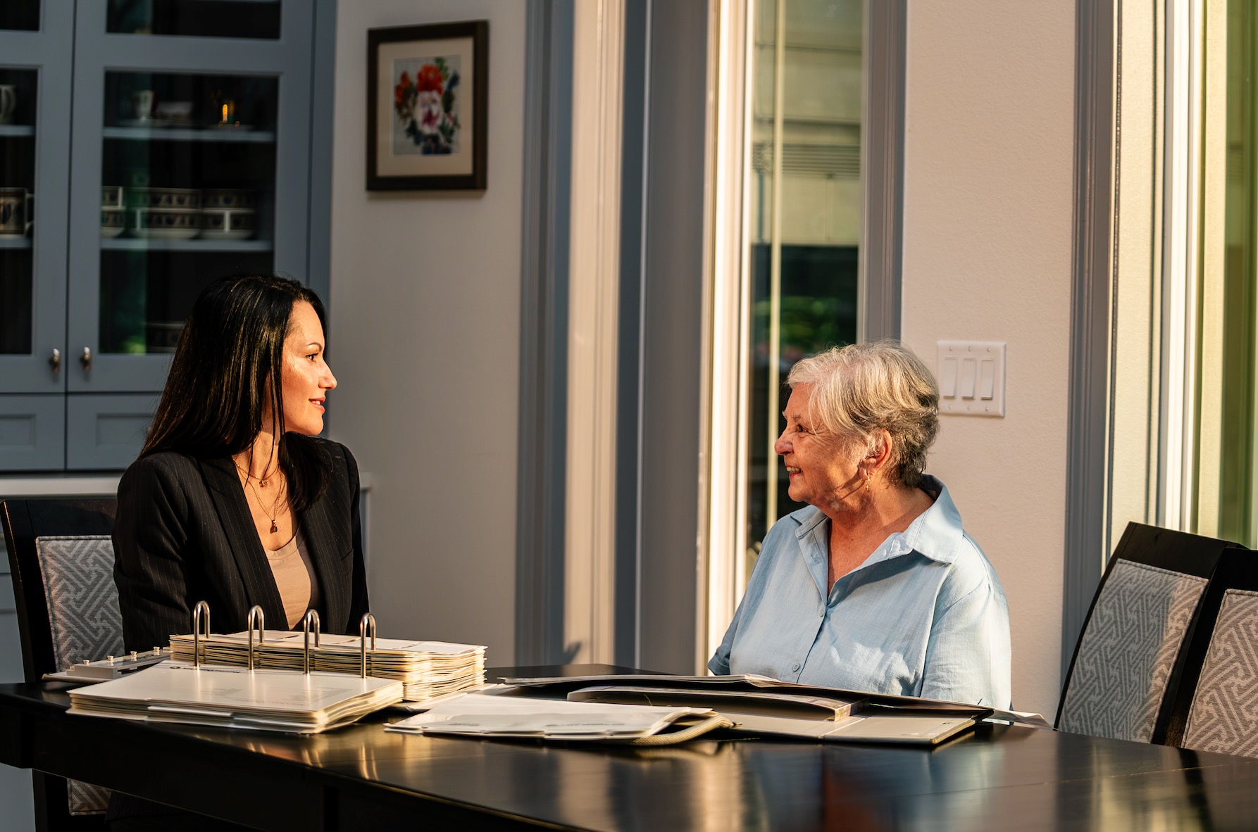 Designer and homeowner talking through window covering options with sample binders in a sunlit dining room