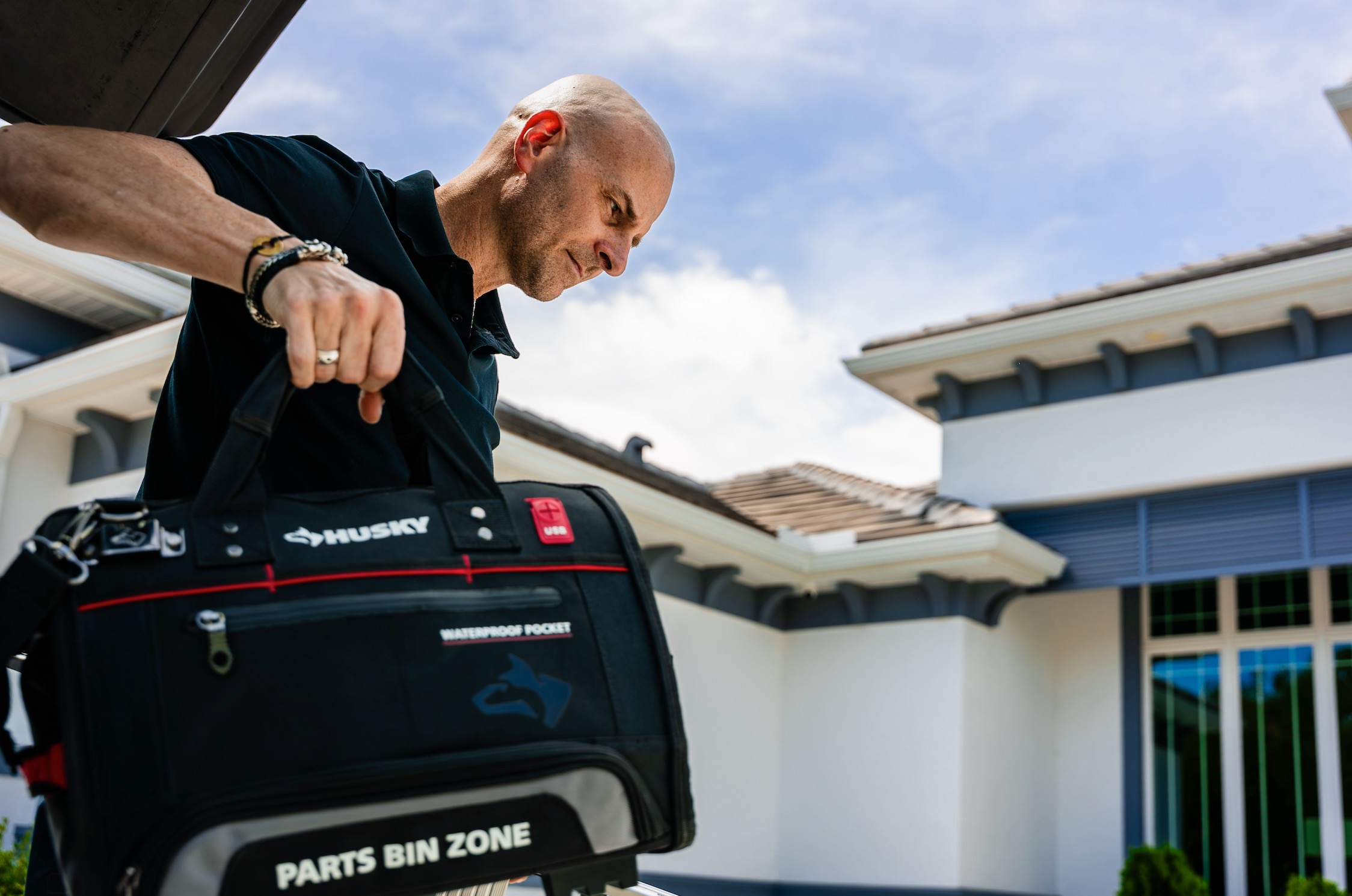Installer lifting a tool bag from his vehicle outside a home before a window treatment install