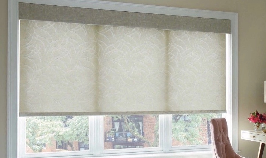 Fabric-covered cornice above a patterned cream roller shade on a triple window