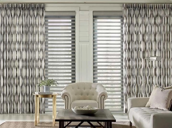 Grey patterned custom drapery panels framing sheer banded shades in a living room