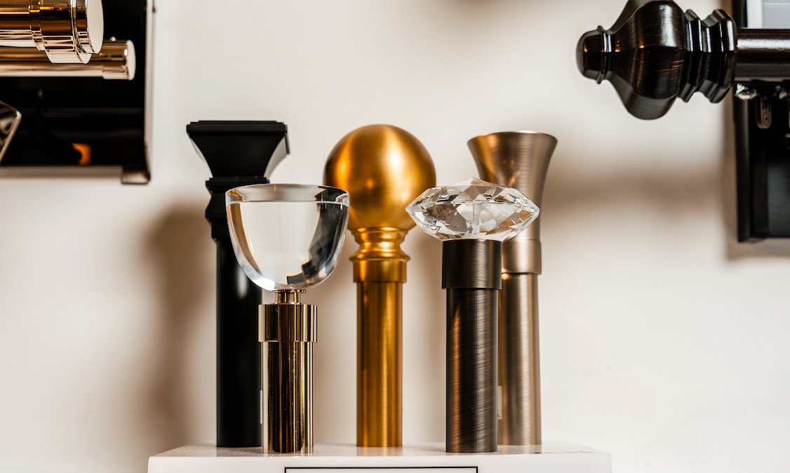 Crystal, brass and brushed-nickel drapery rod finials lined up on a showroom shelf