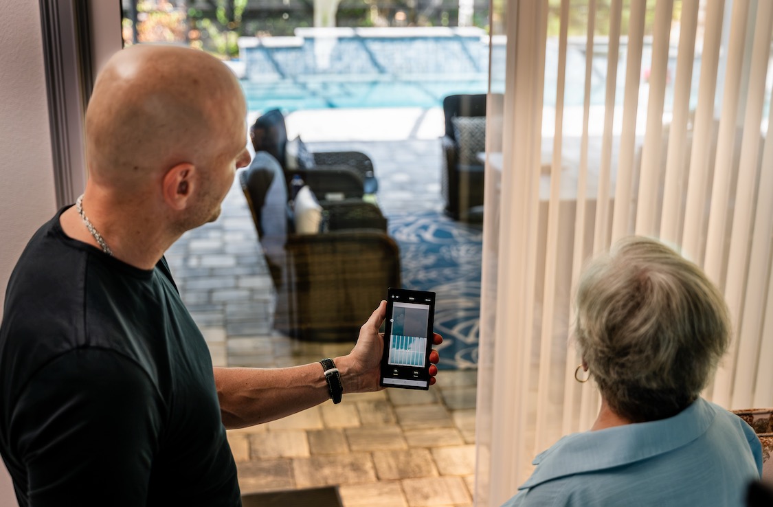 Consultant demonstrating a shade-control app at a sliding door with sheer vertical shades