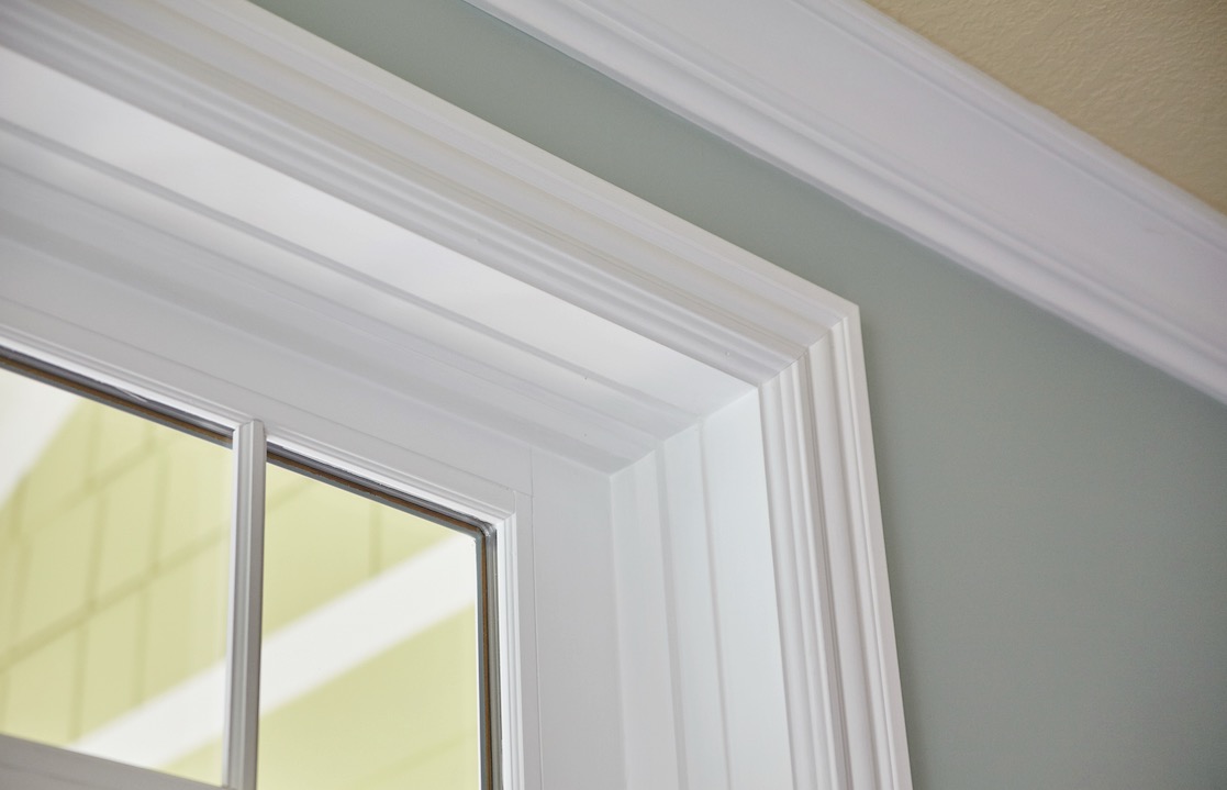 Close-up of layered white window casing and crown molding against a sage green wall