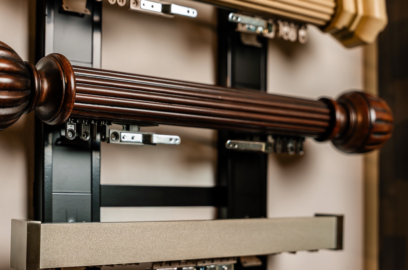 Close-up of a fluted dark wood drapery rod with ball finials and metal traverse tracks behind