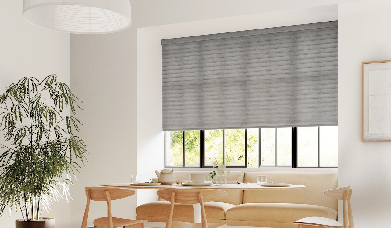 Charcoal pleated shade lowered over a wide dining nook window above a banquette and round wood table