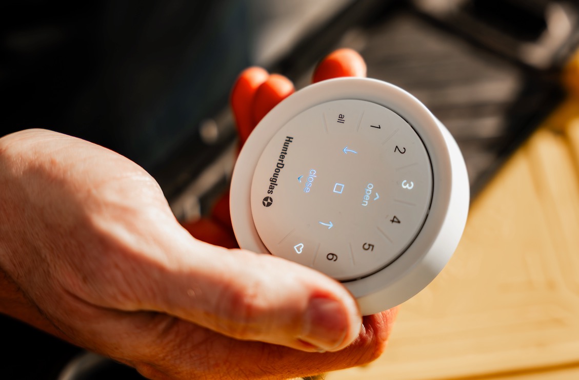 Hand holding a Hunter Douglas PowerView remote with lit open and close controls