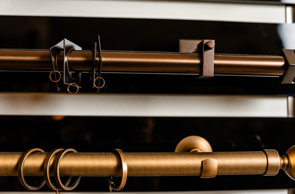 Bronze and brass drapery rods with rings and mounting brackets on a display rack