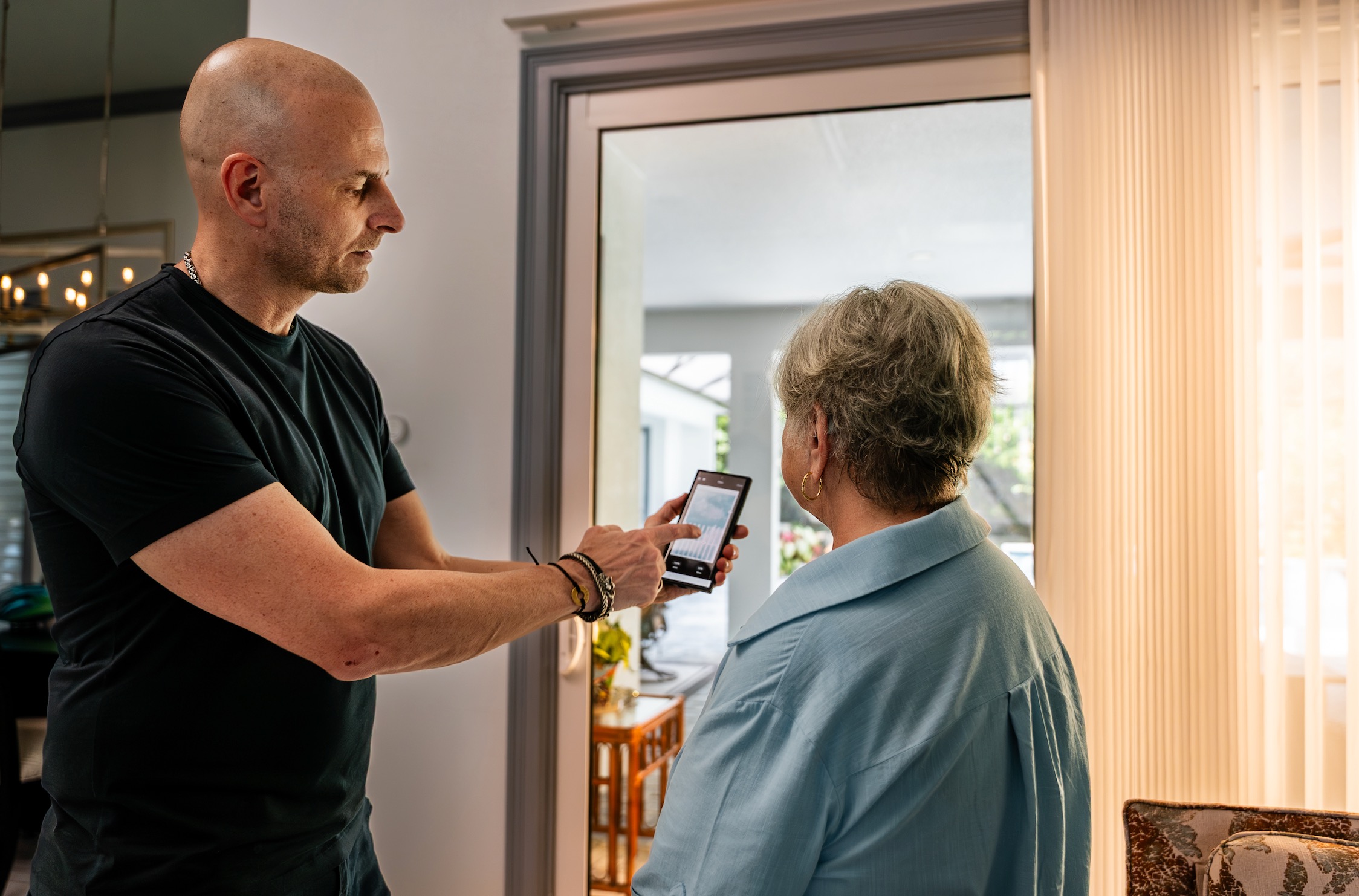 Installer showing a homeowner an app on his phone beside sheer vertical window panels
