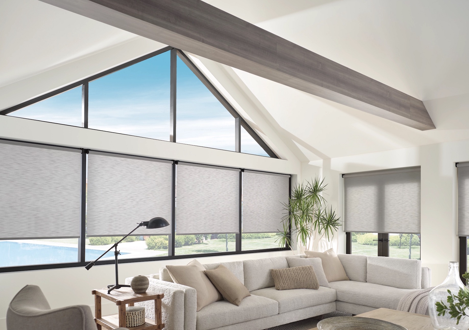 Roller shades on a wall of black-framed windows in a vaulted great room with a triangular gable window