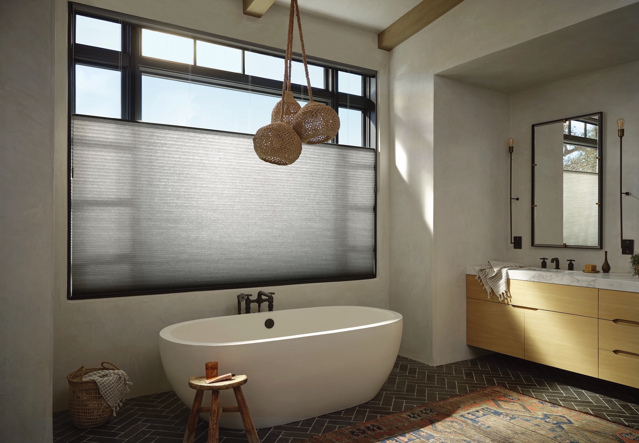 Cellular honeycomb shade on a black-framed bathroom window above a freestanding soaking tub