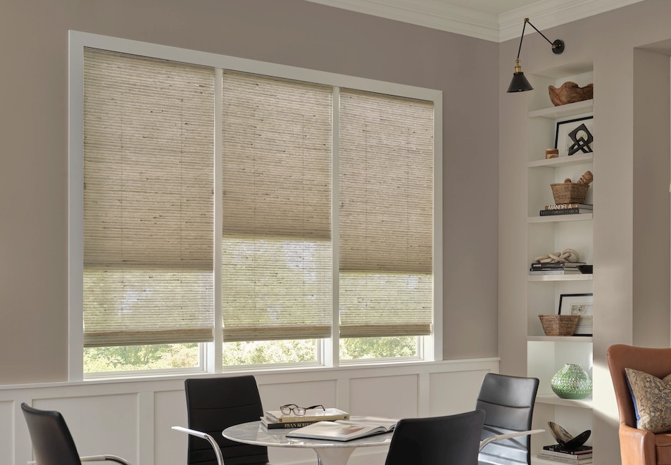 Natural woven wood shades half-raised on a three-panel window above a home office meeting table