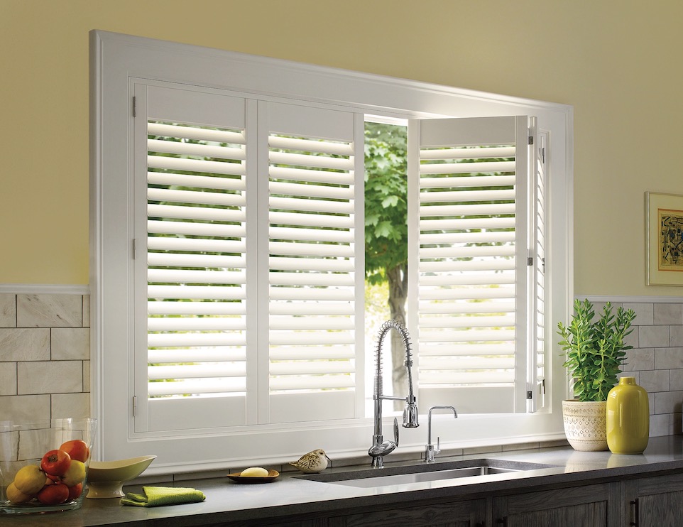 White plantation shutters on a kitchen sink window with one bi-fold panel swung open