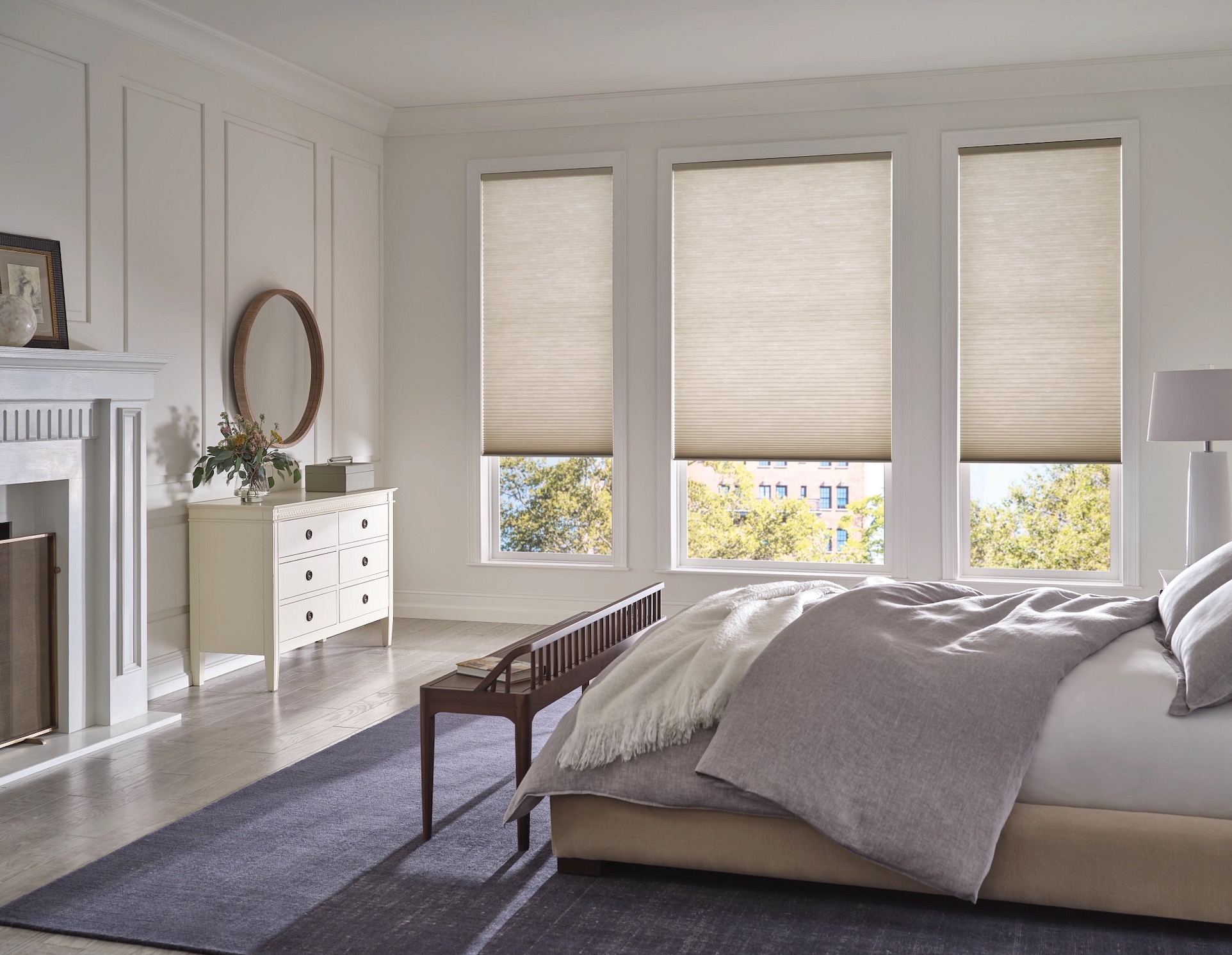 Cream cellular honeycomb shades half-lowered on three bedroom windows above a linen bed