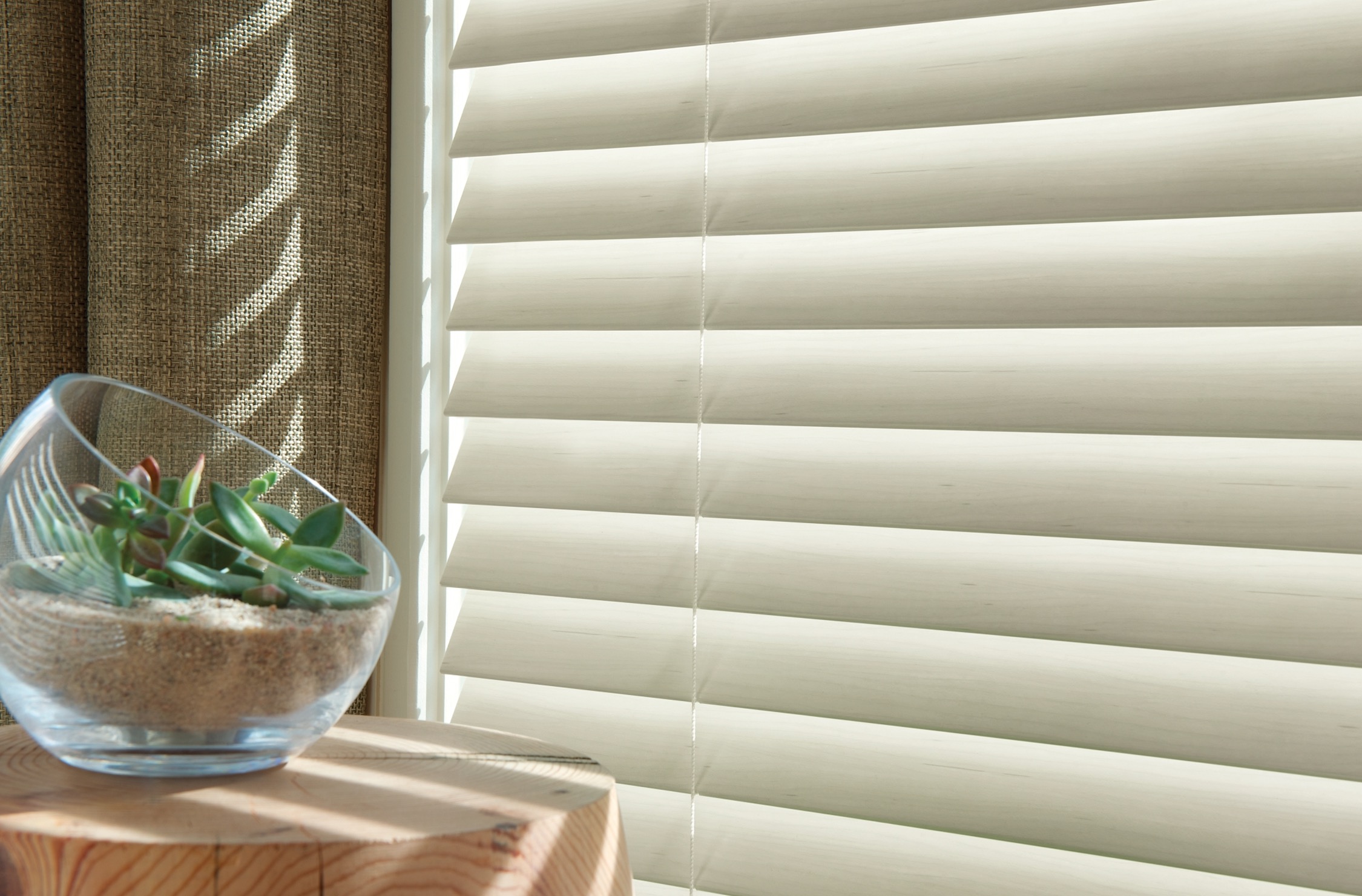 Close-up of cream faux wood blind slats with a succulent bowl on a wood stool