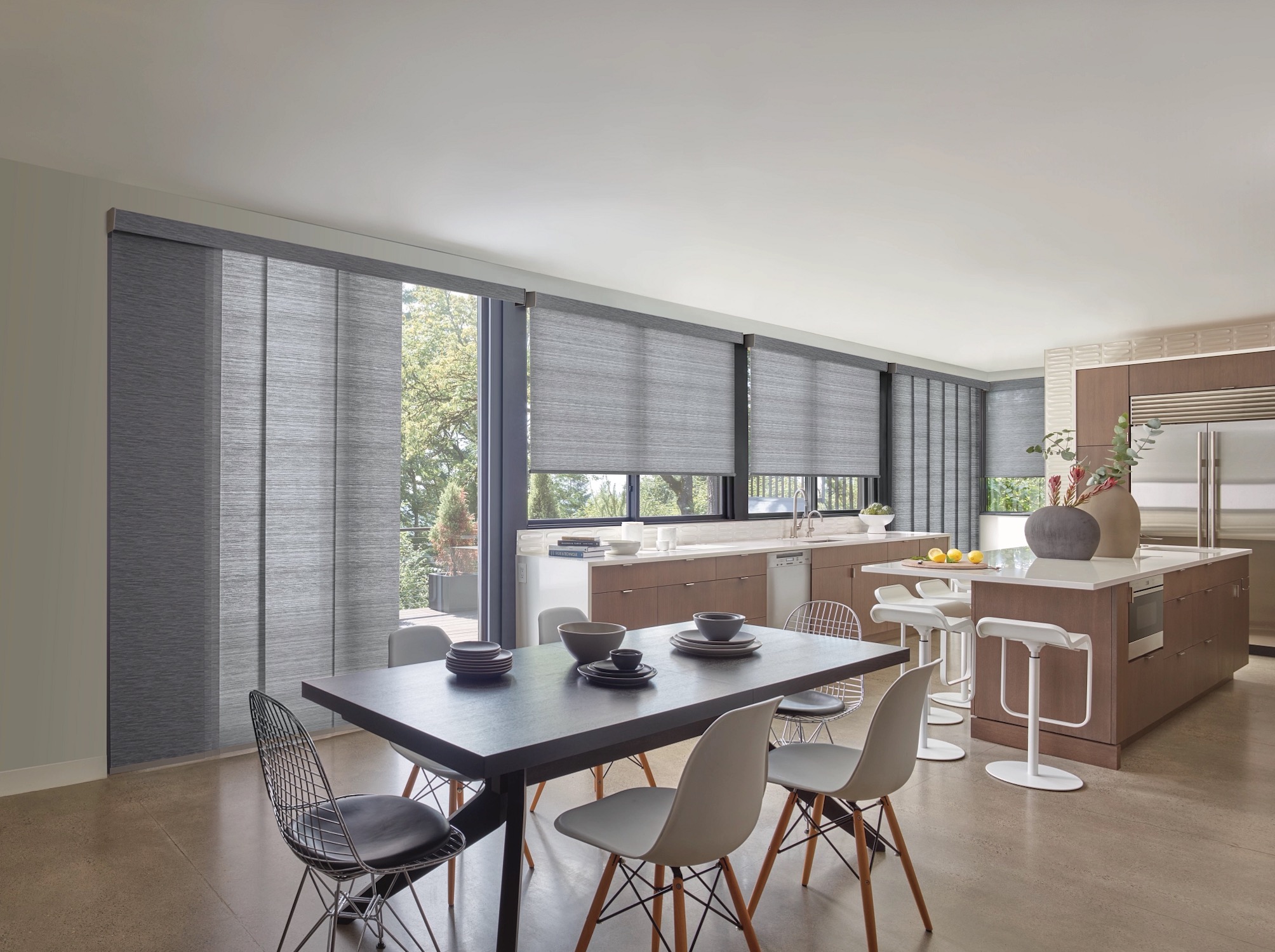 Grey woven roller shades and a sliding panel track over kitchen windows and a patio door