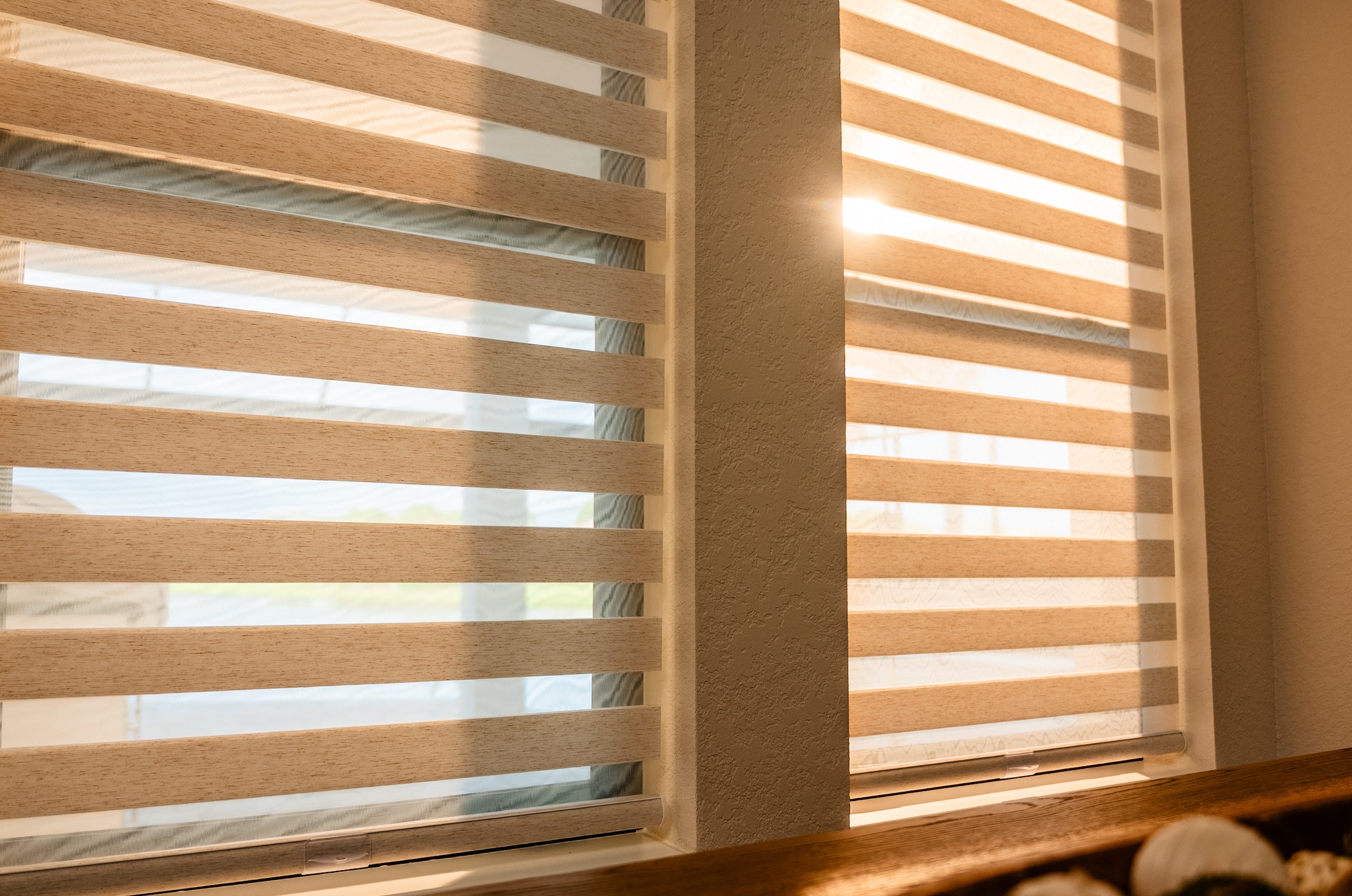 Sunlight filtering through layered banded sheer shades on two adjoining windows