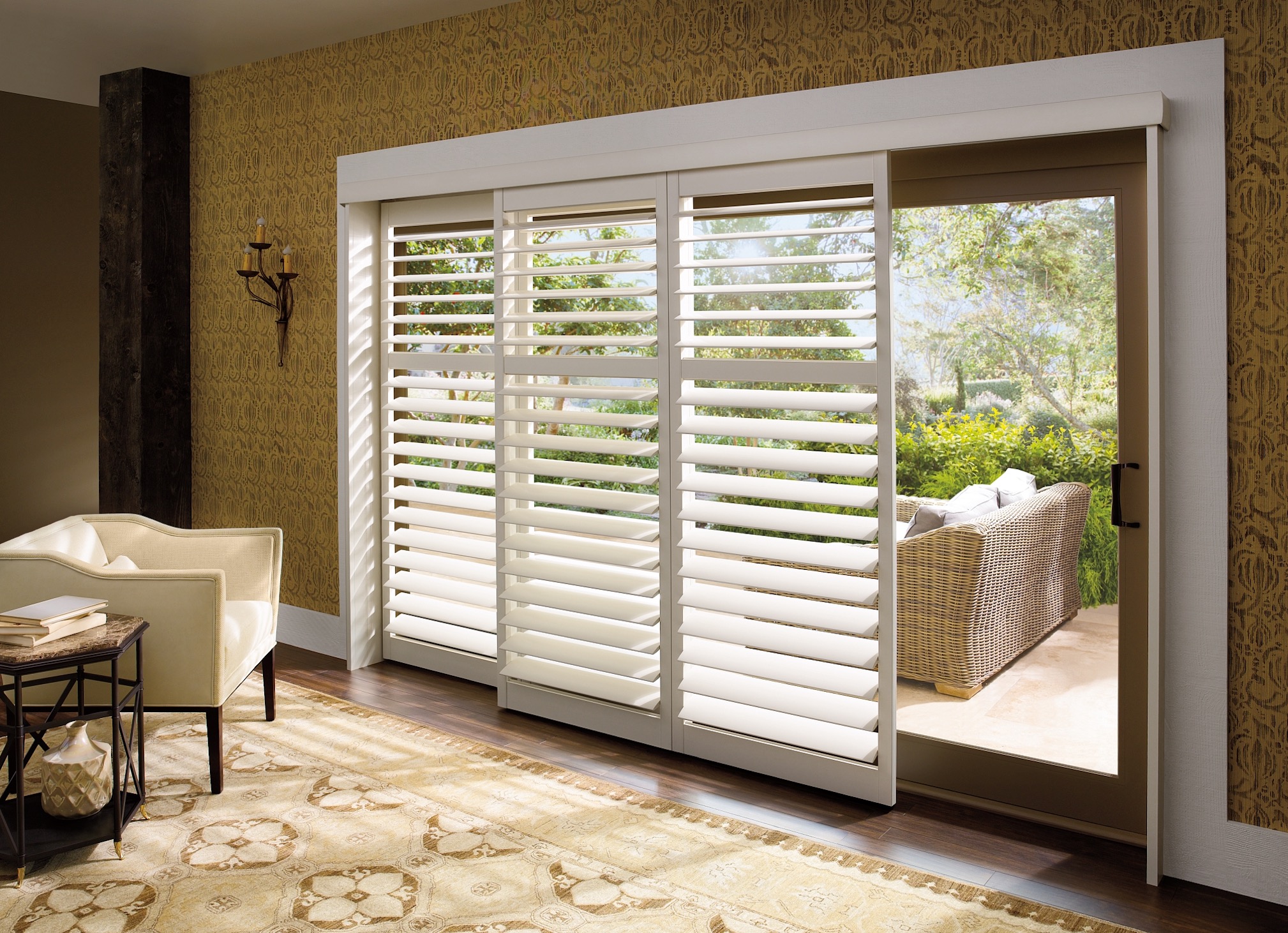 White plantation shutters on a sliding glass patio door, one panel slid open to the patio