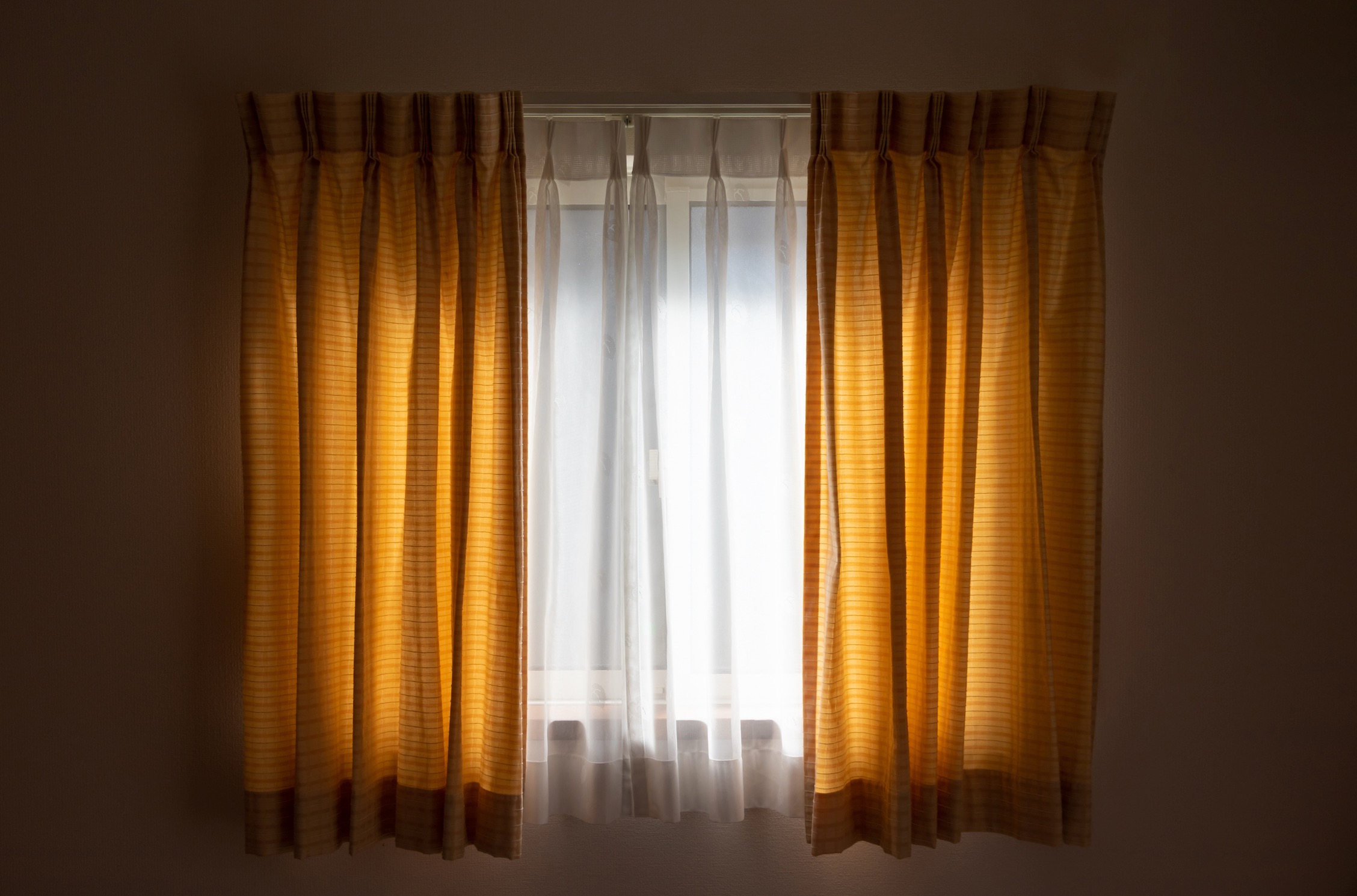 Gold pinch-pleat drapery layered over white sheer curtains at a window