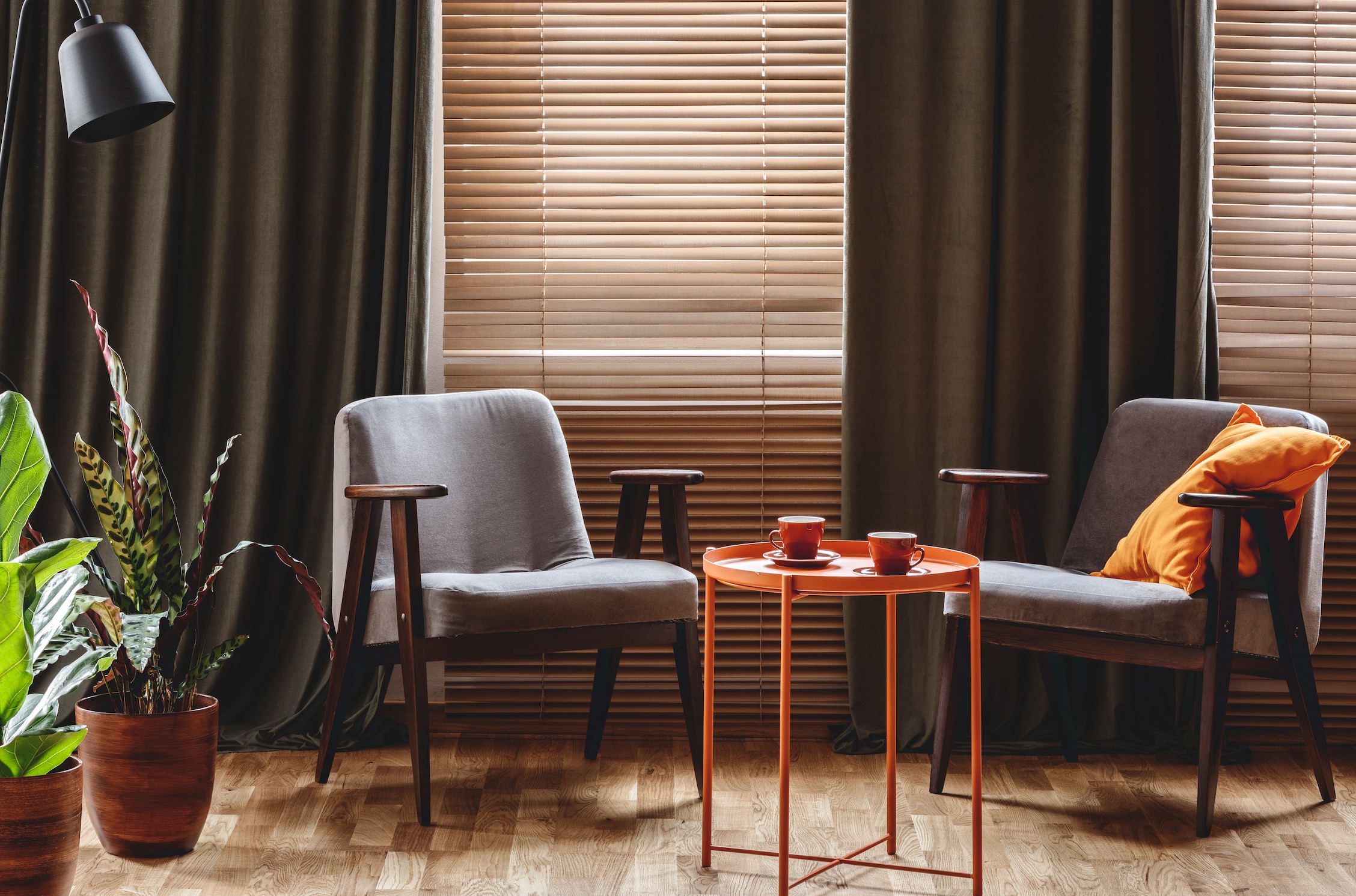 Olive drapery panels framing wood blinds behind two mid-century armchairs