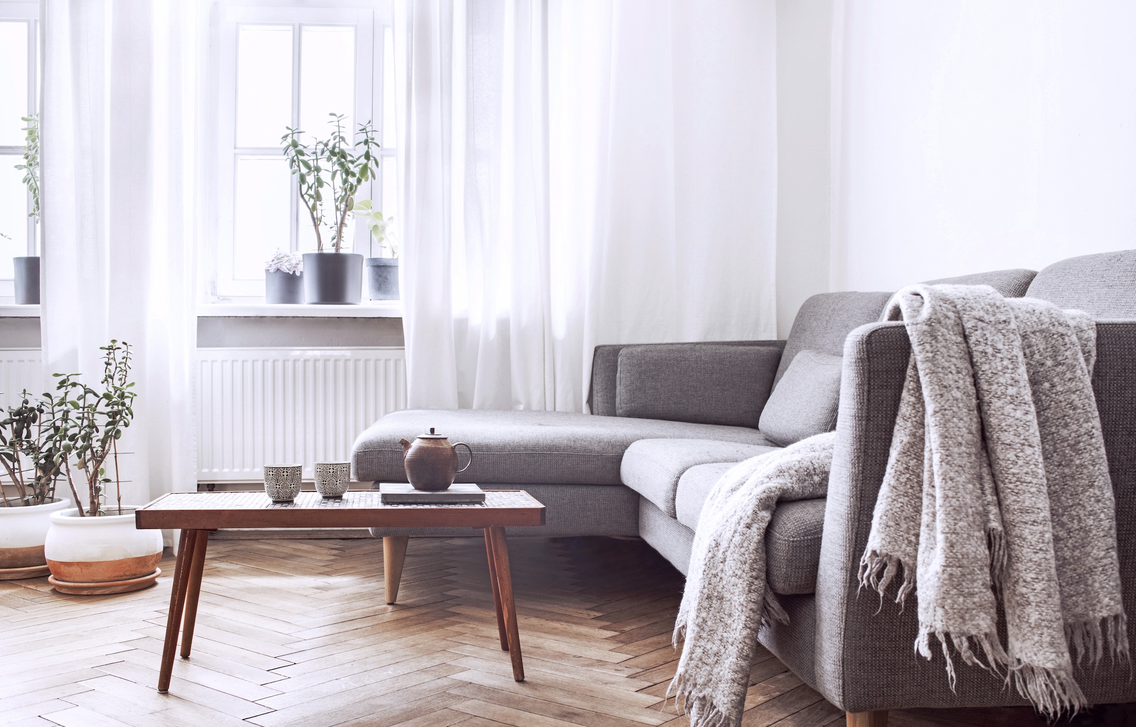 Floor-length white sheer curtains beside a grey sofa in a bright living room