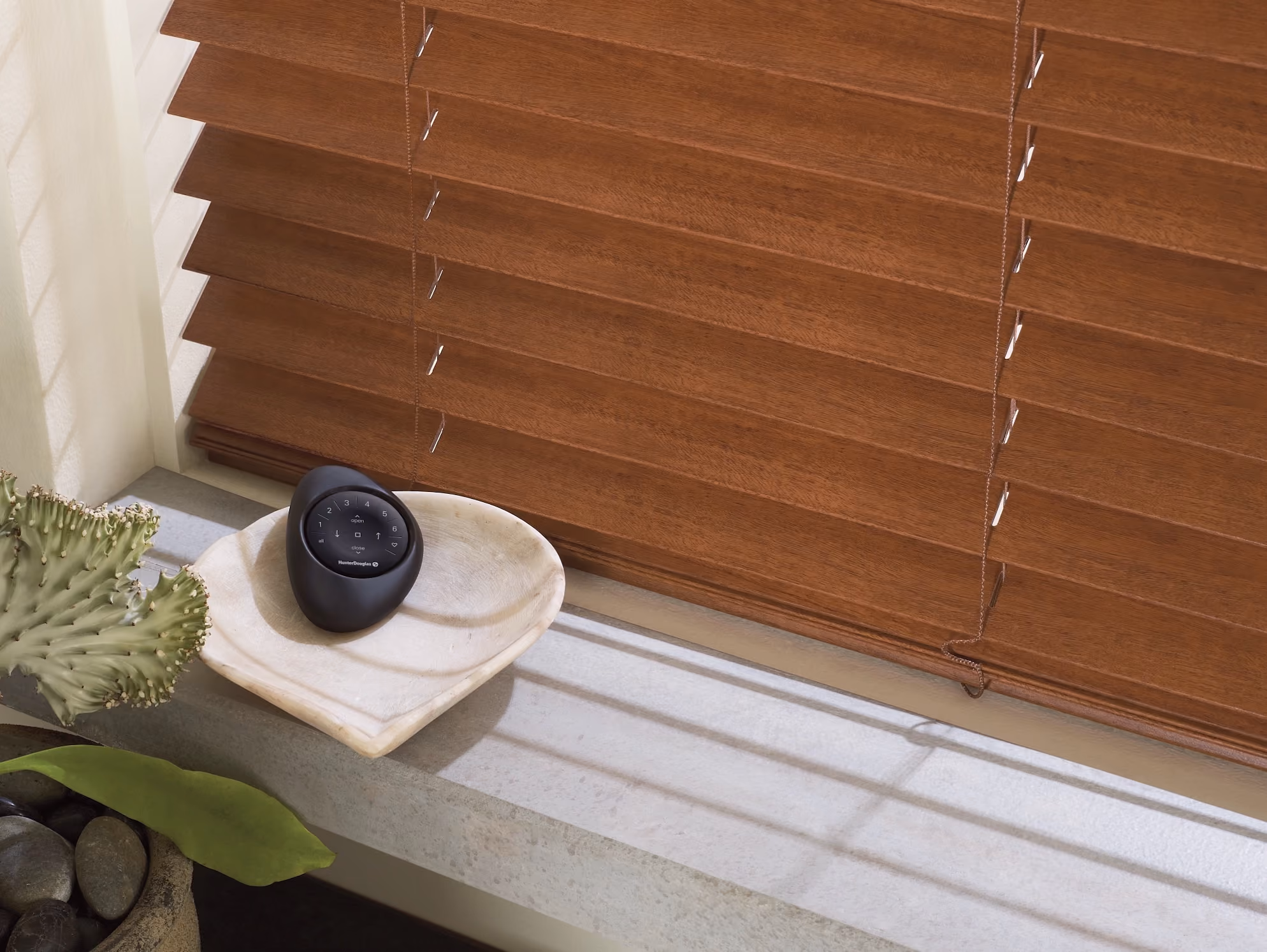 Medium-brown wood blinds with a Hunter Douglas remote resting in a dish on the windowsill