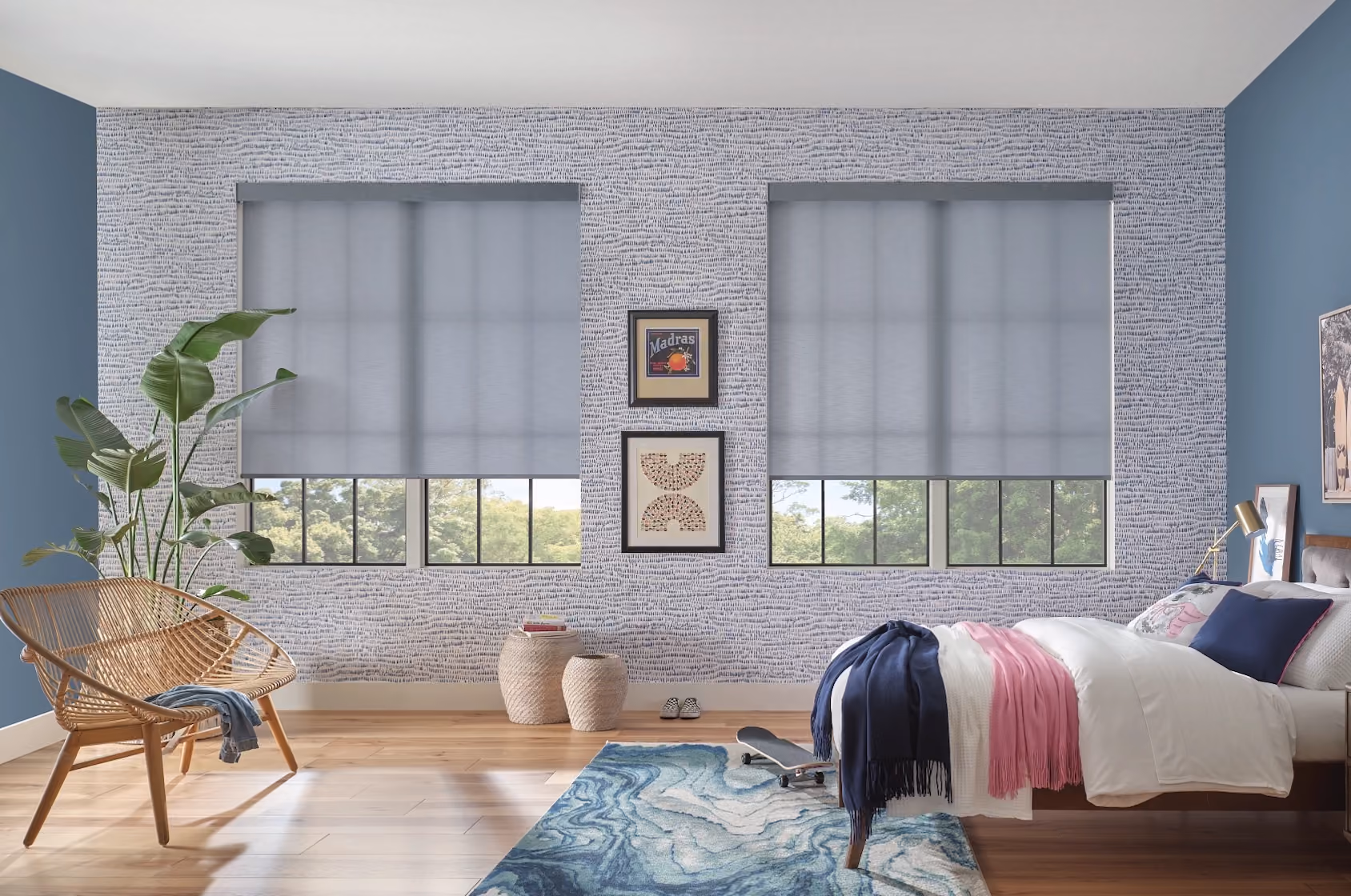 Grey roller shades half-lowered on two windows in a blue kids bedroom with rattan chair and skateboard
