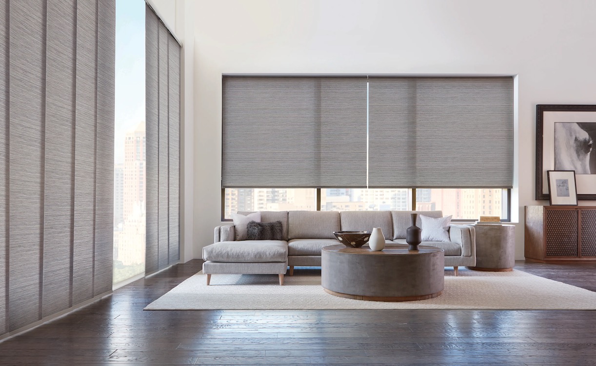 Grey woven vertical panel shades and matching roller shades in a high-rise living room
