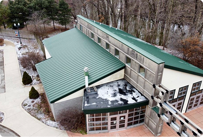 A building with green metal roofs and large windows, surrounded by leafless trees and pathways.