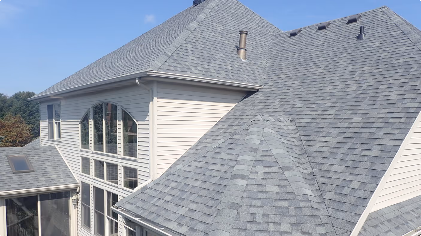 Modern house exterior showing gray shingled roof and multiple windows under a clear blue sky.