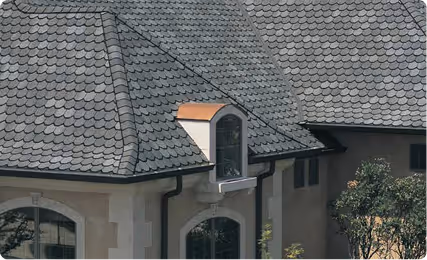 House roof with textured dark gray designer shingles and a small dormer window with a curved top and brown trim.