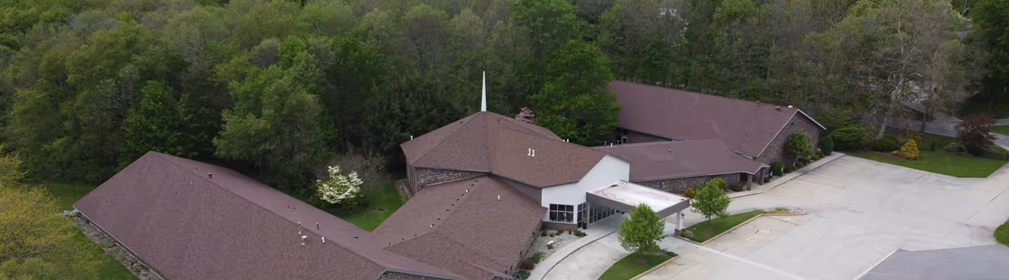 Aerial view of a church building with a white steeple surrounded by trees and parking lots.