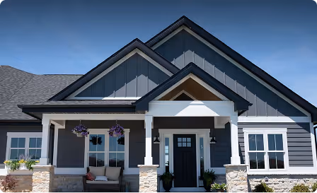 Modern gray house with white trim, front porch, and stone pillars under a clear blue sky.