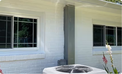 White brick exterior wall with two windows and an air conditioning unit in front.