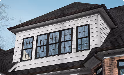 Close-up of a white house dormer with multiple black-framed grid windows under a dark roof.
