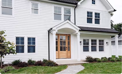 Front view of a modern white two-story house with multiple windows, a wooden double front door, and a curved stone pathway leading to the entrance.