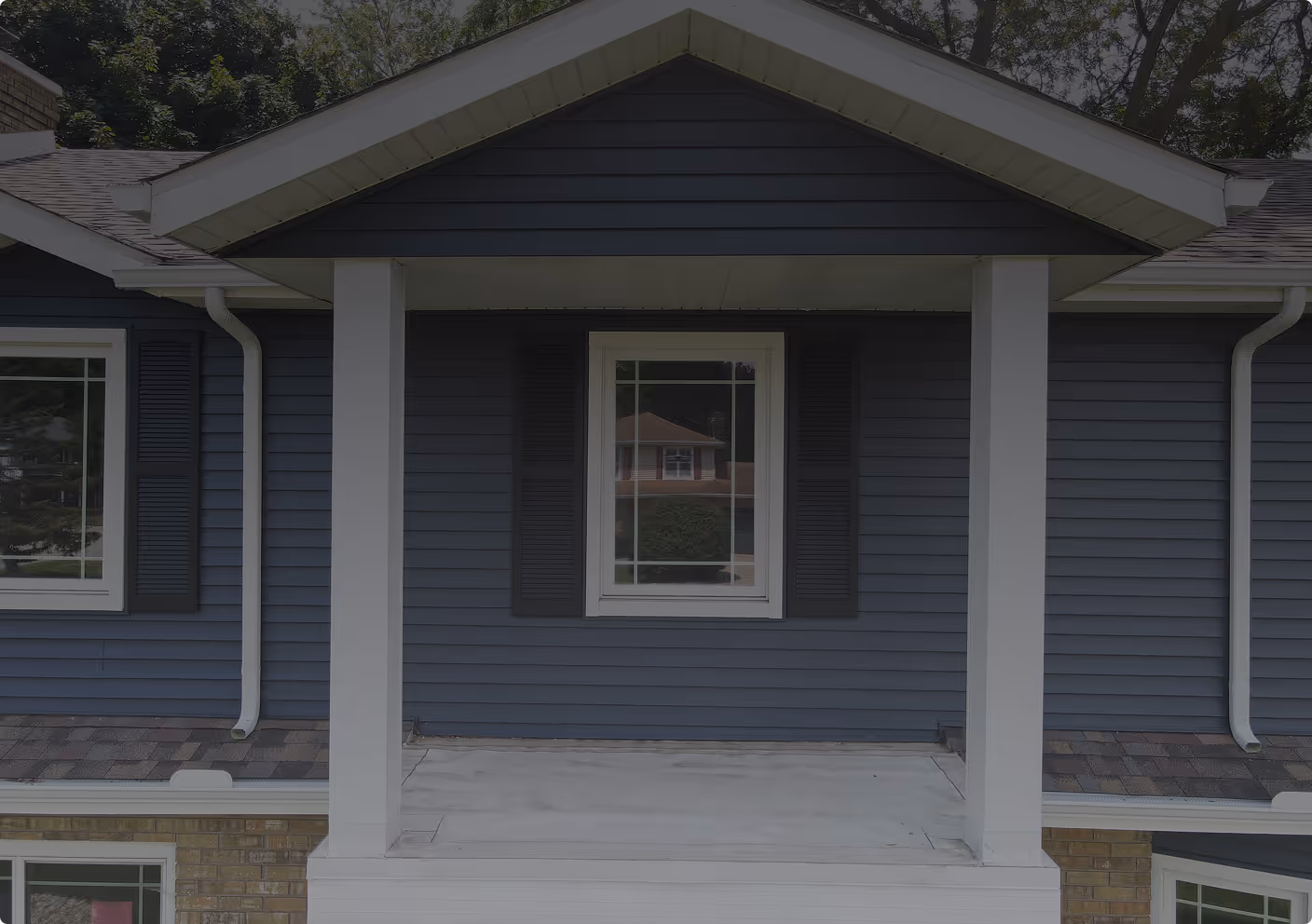 Small front porch with white pillars and a blue house exterior featuring a central window with black shutters.