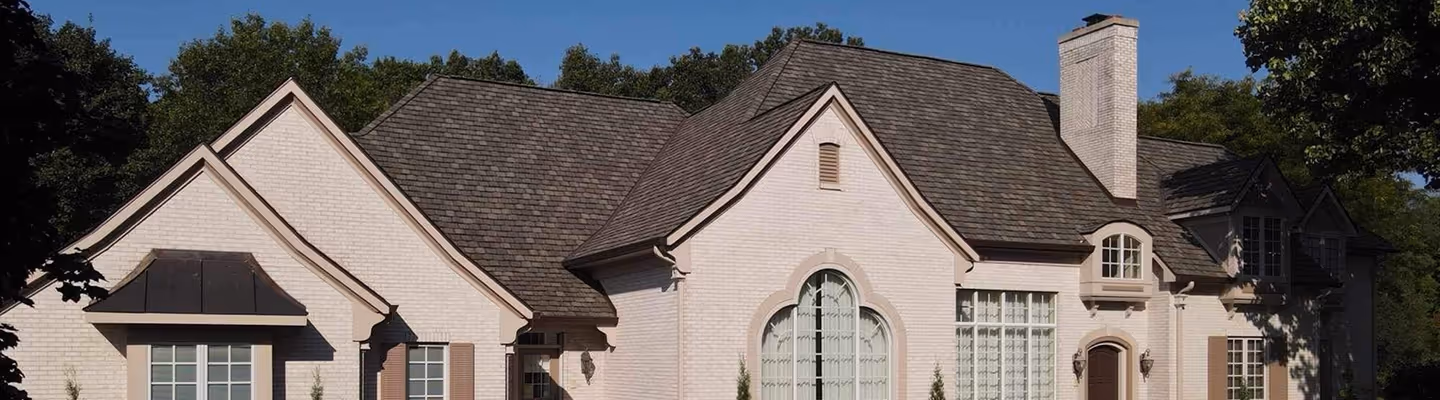 Large light brick house with multiple steep roofs and a chimney under a clear blue sky.