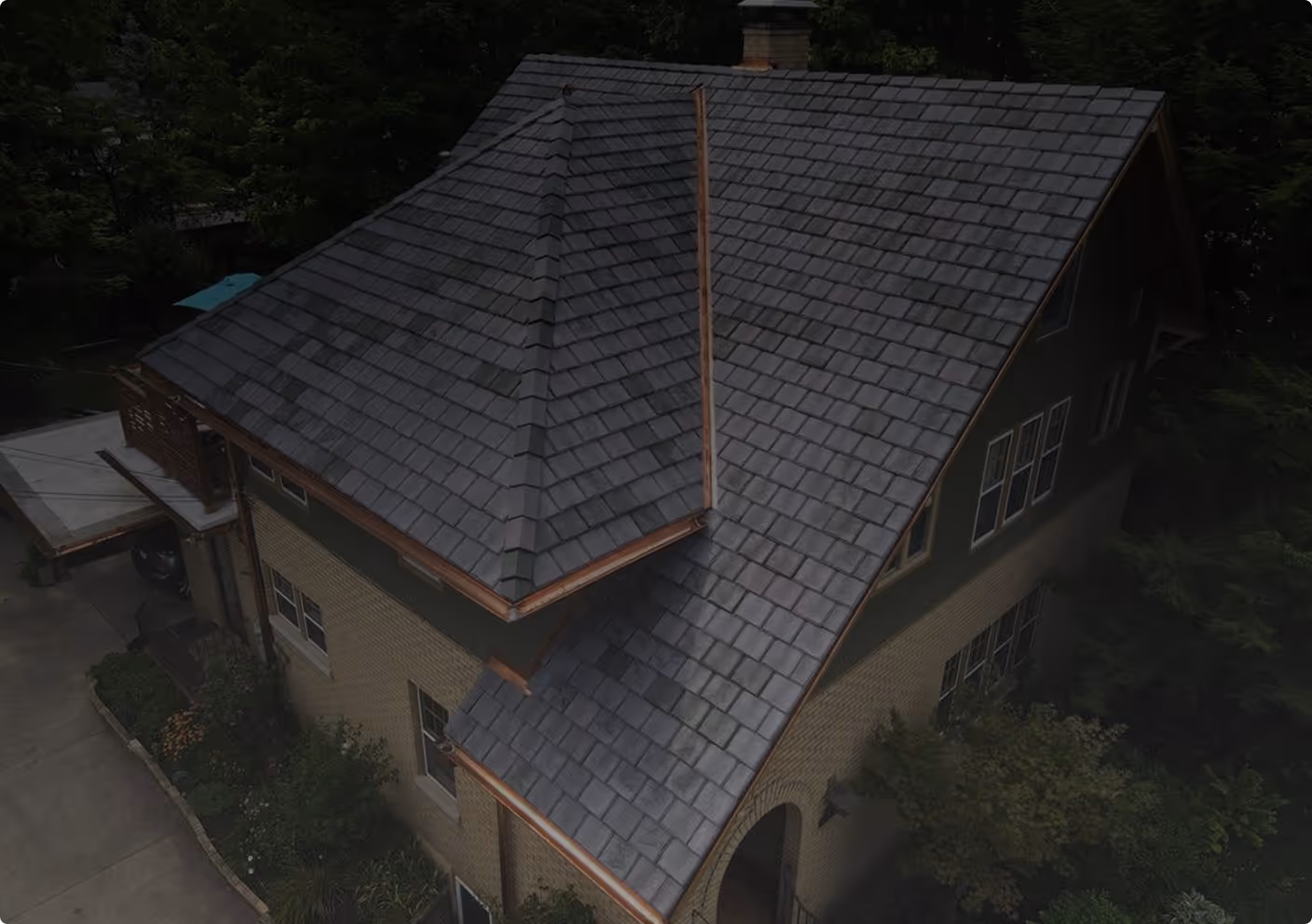 A two-story house with a gray shingled roof and copper gutters, surrounded by trees and greenery.