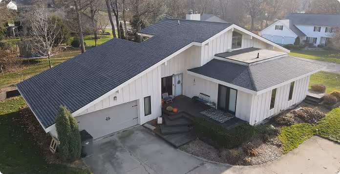 A modern house with a multi-sloped dark gray roof, white exterior walls, and a small front porch with seasonal decorations.